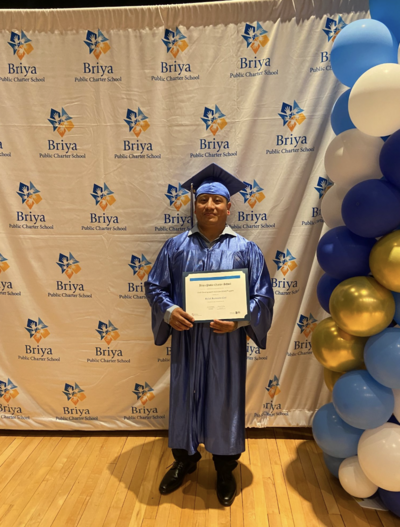 picture of a Briya PCS graduate in front of a step-and-repeat backdrop with balloons on one side