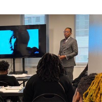 teacher teaching a class while standing by a presentation board