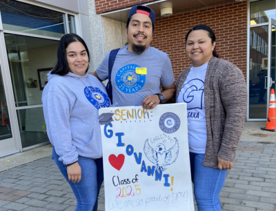 a family of 3 holding a poster that reads "Senior, Giovanni, Class of 2025, We Are So Proud of You"