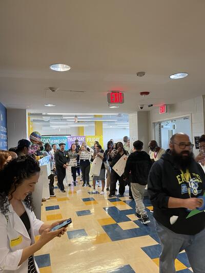 parents lining the walls of a school hallway, almost every person is holding a sign for their scholar